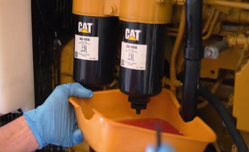 A hand in blue gloves uses a pan to catch fluid while handling CAT filters, a key fuel-saving tip for diesel generator maintenance.